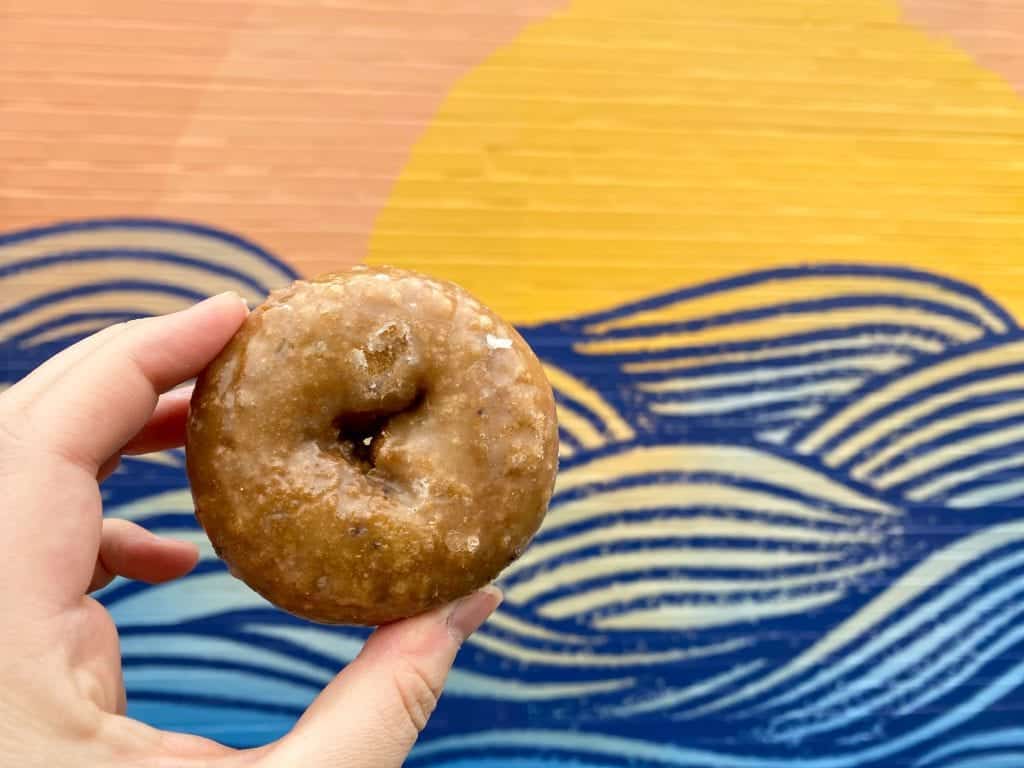Blueberry cake donut held up in front of a mural.